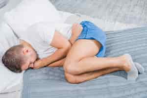 Bezpłatne zdjęcie zasięrzutny widok mężczyzna lying on the beach na łóżku ma żołądek obolałość