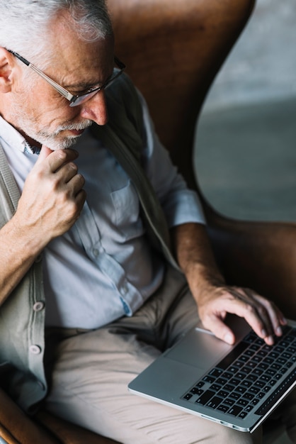 Zasięrzutny widok starszego mężczyzna obsiadanie na krześle używa laptop