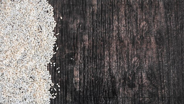 Bezpłatne zdjęcie zasięrzutny widok uncooked biali ryż na czarnym drewnianym textured tle