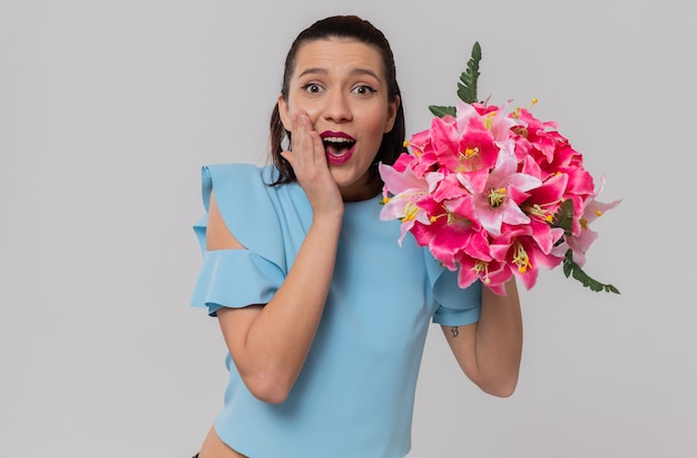 Zaskoczona ładna młoda kobieta trzymająca bukiet kwiatów i kładąca dłoń na twarzy