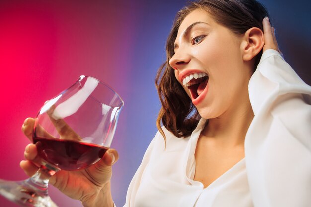 Zaskoczona młoda kobieta w strojach imprezowych pozuje przy lampce wina.