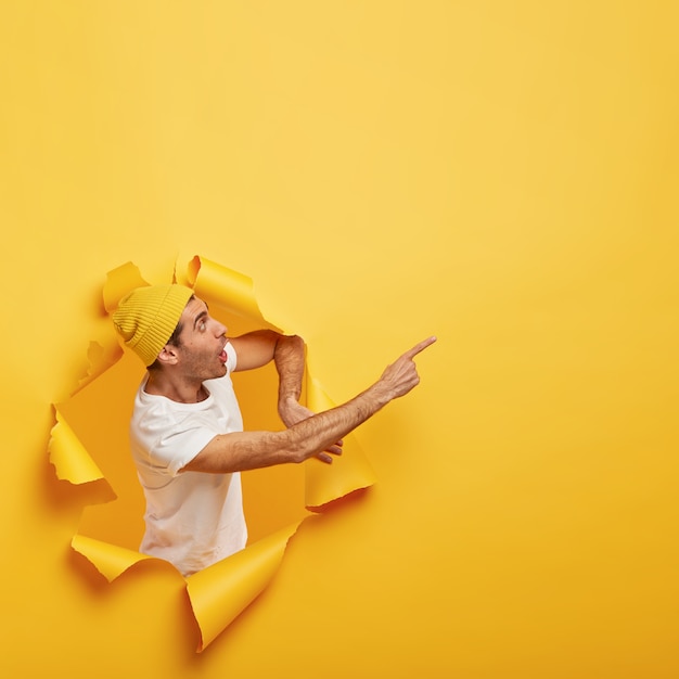 Zaskoczony emocjonalnie facet stoi w papierowej dziurze z podartymi żółtymi krawędziami, demonstrując niesamowitą przestrzeń na kopię