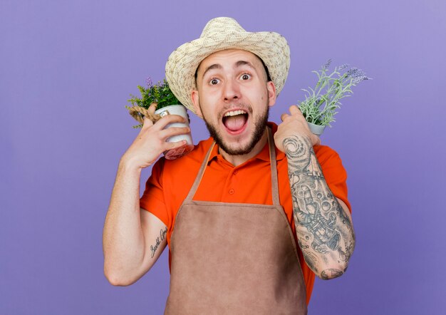 Zaskoczony męski ogrodnik w kapeluszu ogrodniczym trzyma doniczki na ramionach