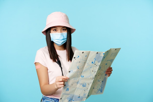 Zaszczepiona koreańska kobieta w medycznej masce na twarz trzymająca mapę turystyczną odwiedzającą zwiedzanie w podróży