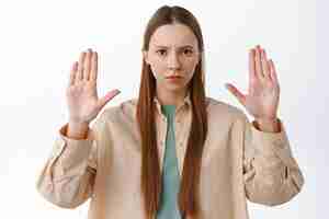 Bezpłatne zdjęcie zatrzymaj to, trzymaj się z daleka, trzymaj się z daleka. poważnie marszcząca brwi dziewczyna pokazująca gest blokowania, mówi „nie podnosić rąk”, aby zabronić zabronić czemuś odmowy stania nad białym tłem