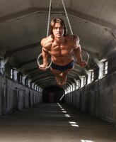 Bezpłatne zdjęcie zawodowy sportowiec o pięknym muskularnym ciele trenuje na kółkach gimnastycznych w opuszczonym budynku przemysłowym