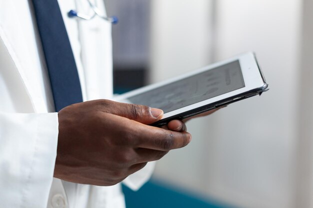 Zbliżenie african american lekarz analizowanie wiedzy o chorobach za pomocą tabletu monitorującego objawy pacjenta podczas badania klinicznego. Terapeuta pracujący przy leczeniu w gabinecie szpitalnym