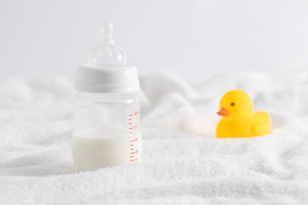 Zbliżenie butelka pełna mleka obok kaczki zabawki na białej powierzchni