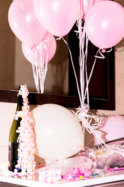 Zbliżenie butelki szampana z konfetti i różowe balony na biurku