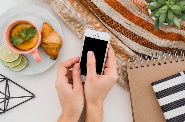 Bezpłatne zdjęcie zbliżenie dłoni kobiety za pomocą telefonu komórkowego ze śniadaniem i herbaty cytrynowej na białym tle