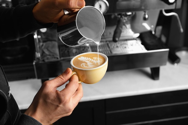 Bezpłatne zdjęcie zbliżenie dłoni wlewając mleko w filiżankę pysznej kawy