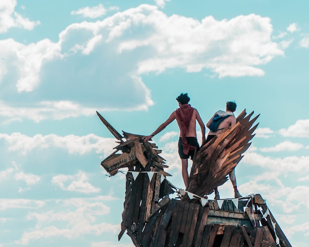 Zbliżenie dwóch mężczyzn stojących na posągu jednorożca wykonanym z desek z drewna na pochmurnym niebie