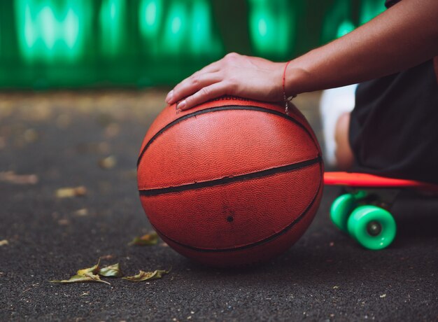 Zbliżenie fotografii koszykówki piłka z dziewczyny obsiadaniem na plastikowym pomarańczowym centu shortboard na asfalcie
