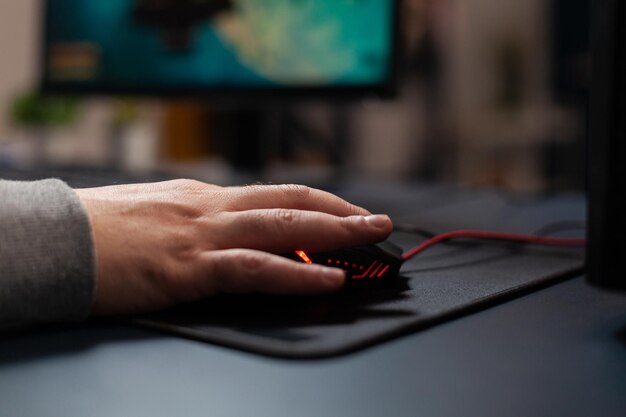 Zbliżenie gracza trzymającego mysz na podkładce, aby grać w gry wideo. Człowiek za pomocą sprzętu do gier na komputerze, grając w gry online przy biurku. Ręka gracza na gadżecie bawiącym się grami