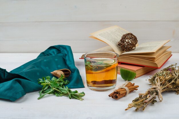 Zbliżenie herbaty ziołowej i kwiatów z książkami, cytryną, przyprawami i zielonym szalikiem