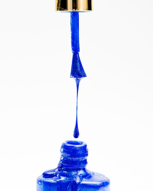 Zbliżenie: jasny brokat niebieski lakier do paznokci kapie z pędzla w butelce