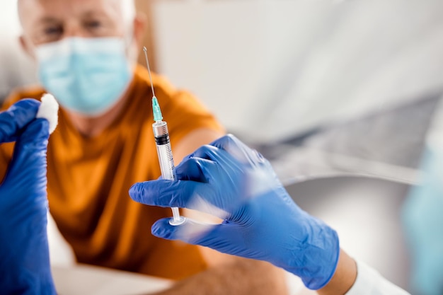 Zbliżenie lekarza przygotowującego szczepionkę dla starszego pacjenta w klinice