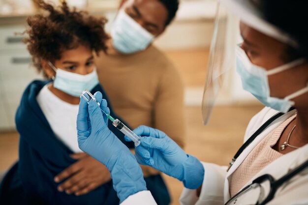 Zbliżenie lekarza używającego strzykawki i przygotowującego lek dla dziecka podczas pandemii koronawirusa