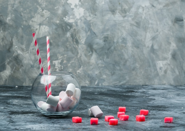 Zbliżenie marshmallows i cukierek w słoiku z cukierkami i czerwonym obrusem w kratkę na ciemnoniebieskiej i szarej marmurowej powierzchni. wolne miejsce w poziomie na tekst