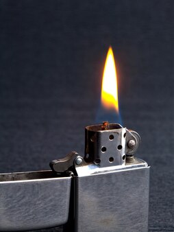 Zbliżenie metalowej zapalniczki gazowej z płonącym ogniem na szarym tle z miejscem na kopię