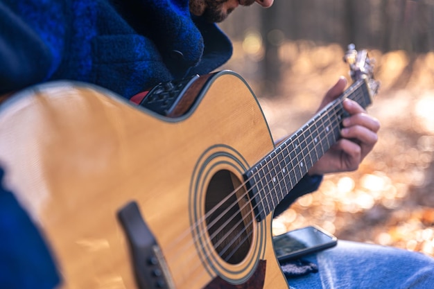Bezpłatne zdjęcie zbliżenie mężczyzna gra na gitarze akustycznej w jesiennym lesie