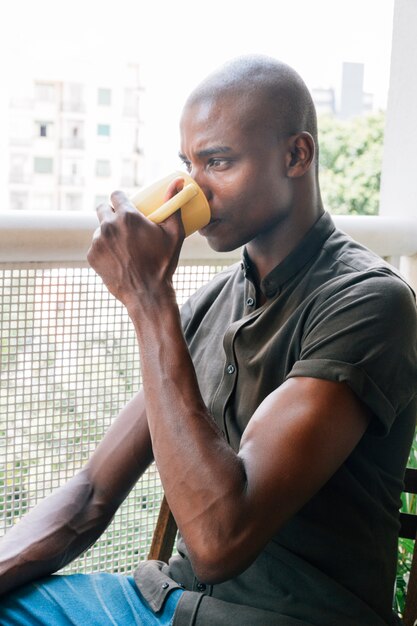 Zbliżenie: mięśni młody człowiek Afryki picia kawy siedząc na balkonie