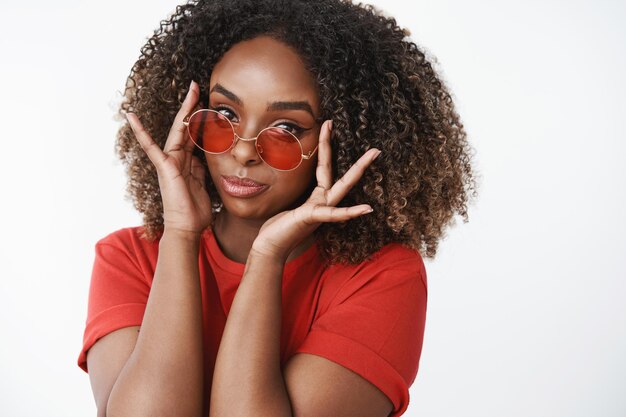 Zbliżenie modnej i glamour przystojnej afroamerykańskiej kobiety w dorywczo czerwonej koszulce zakładającej stylowe okulary z czerwonym kółkiem