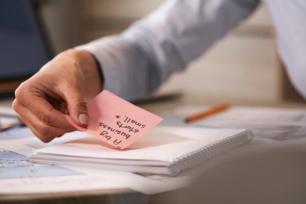 Zbliżenie na bizneswoman stosującą inspirującą kartkę samoprzylepną na swoim notatniku podczas pracy w biurze