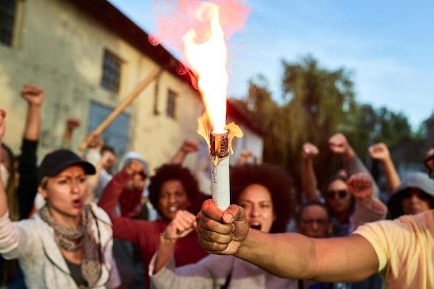 Zbliżenie na demonstranta trzymającego zapaloną pochodnię, podczas gdy tłum ludzi krzyczy w tle