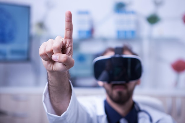Zbliżenie na lekarza, wskazując w powietrzu palcem na sobie zestaw wirtualnej rzeczywistości. Lekarz w mundurze medycznym.