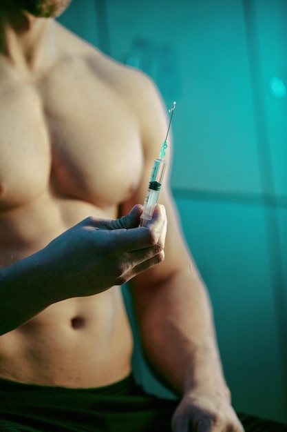Zbliżenie na muskularnego mężczyznę z zastrzykiem sterydów anabolicznych w szatni siłowni