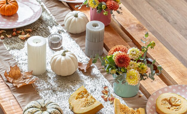 Zbliżenie na przytulne detale wystroju świątecznego jesiennego stołu z dyniami, kwiatami i świecami.