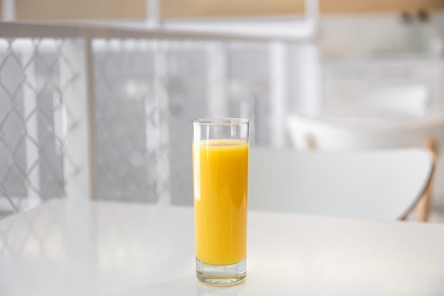 Zbliżenie na szklankę soku pomarańczowego na niewyraźne jasne tło wnętrza kawiarni.