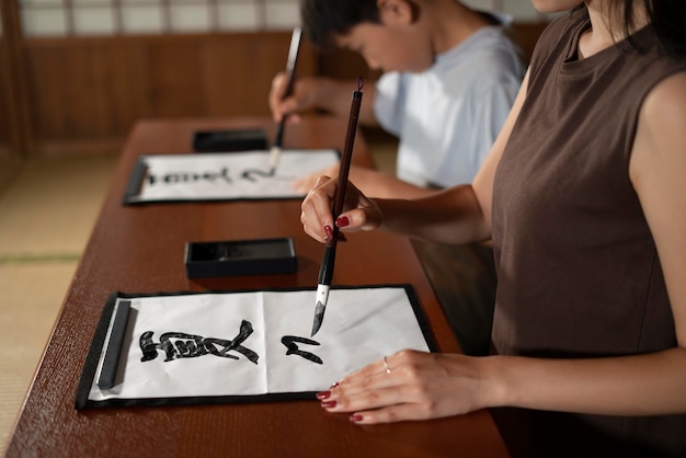 Zbliżenie na uczniów wykonujących japońską kaligrafię, zwaną shodo