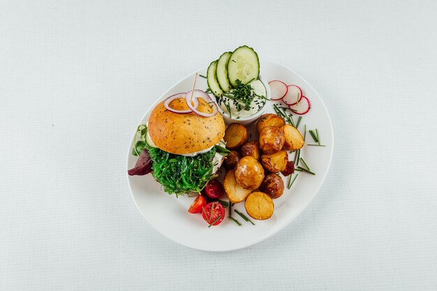 Zbliżenie na widok z góry pieczonych ziemniaków z pomidorem i rzodkiewką obok burgera z rukolą