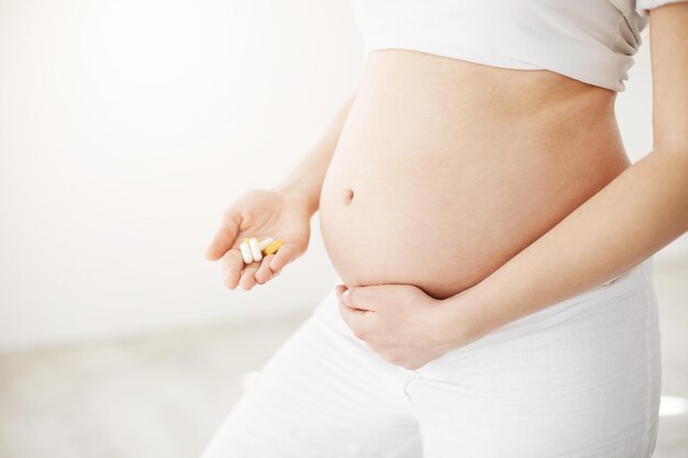 Zbliżenie na wkrótce szczęśliwą matkę trzymającą tabletki na brzuch i prenatalne oraz witaminy i minerały czekające na zdrowe dziecko Koncepcja prenatalna Wysoki klucz