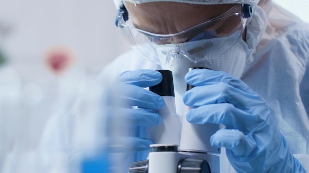 Zbliżenie naukowiec lekarz patrząc pod mikroskopem medycznym analizując próbkę krwi podczas eksperymentu naukowego w laboratorium biochemii. Badacz opracowujący szczepionkę przeciwko Covid19