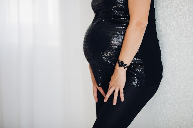 Zbliżenie: nie do poznania kobiety w ciąży w stylowej czarnej musującej górze obejmującej jej brzuch z dwoma ramionami na białym tle. Miejsce.