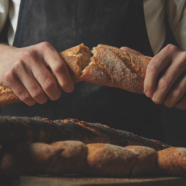 Zbliżenie organiczne pyszne połówki bagietki w rękach mężczyzny na tle czarny fartuch i brązowy drewniany stół