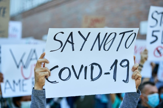 Zbliżenie osoby trzymającej transparent z napisem „NIE” dla COVID19 na proteście podczas epidemii koronawirusa