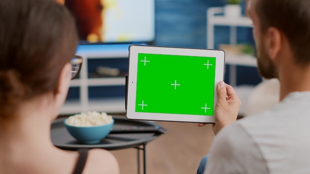 Zbliżenie para trzymająca cyfrowy tablet z zielonym ekranem oglądając webinarium i rozmawiając