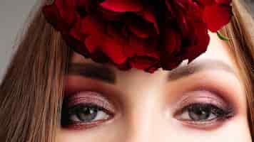 Bezpłatne zdjęcie zbliżenie piękna żeńska górna część twarzy młoda brunetka dziewczyna ukrywa nos i usta za czerwonymi kwiatami ładna dama z jasnym makijażem trzyma róże koncepcja reklamy kosmetyków