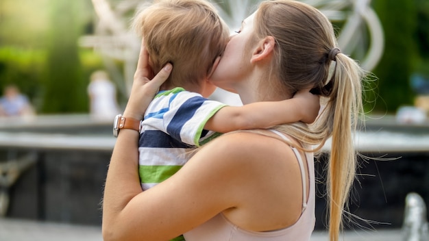 Zbliżenie portret młodej matki przytulanie i pieszcząc jej płacz małego chłopca w parku