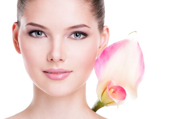 Zbliżenie portret pięknej młodej kobiety ładnej zdrowej skóry i różowe kwiaty w pobliżu twarzy - na białym tle.