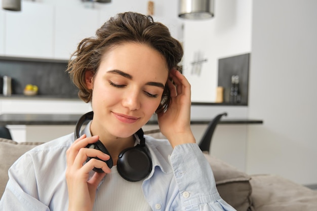 Zbliżenie portretu kobiety lubiącej słuchać muzyki w słuchawkach, siedzącej w domu na sofie