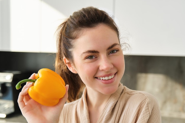 Bezpłatne zdjęcie zbliżenie portretu pięknej kobiety uśmiechającej się, pokazującej wegetariańską dziewczynę z żółtej papryki przygotowującej obiad