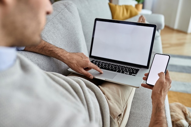 Zbliżenie pracownika zewnętrznego korzystającego z telefonu komórkowego i laptopa podczas relaksu na kanapie w domu