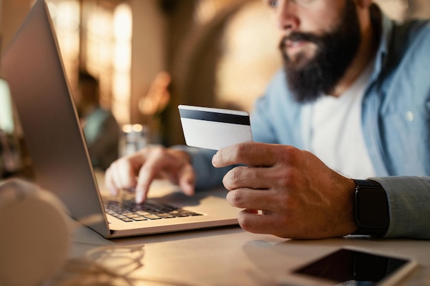 Zbliżenie przedsiębiorcy korzystającego z komputera i karty kredytowej do robienia zakupów w Internecie podczas pracy do późna w biurze