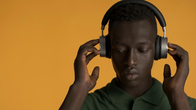 Bezpłatne zdjęcie zbliżenie przystojny afroamerykanin, wyglądający poważnie słuchając muzyki w słuchawkach na żółtym tle