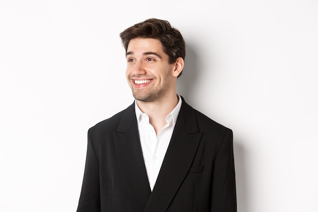Zbliżenie: przystojny mężczyzna przedsiębiorca w garniturze, patrząc w lewo i uśmiechnięty, stojąc na białym tle.